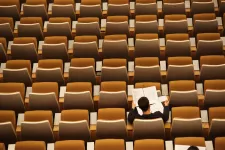 A man sitting alone and reading in an auditorium.